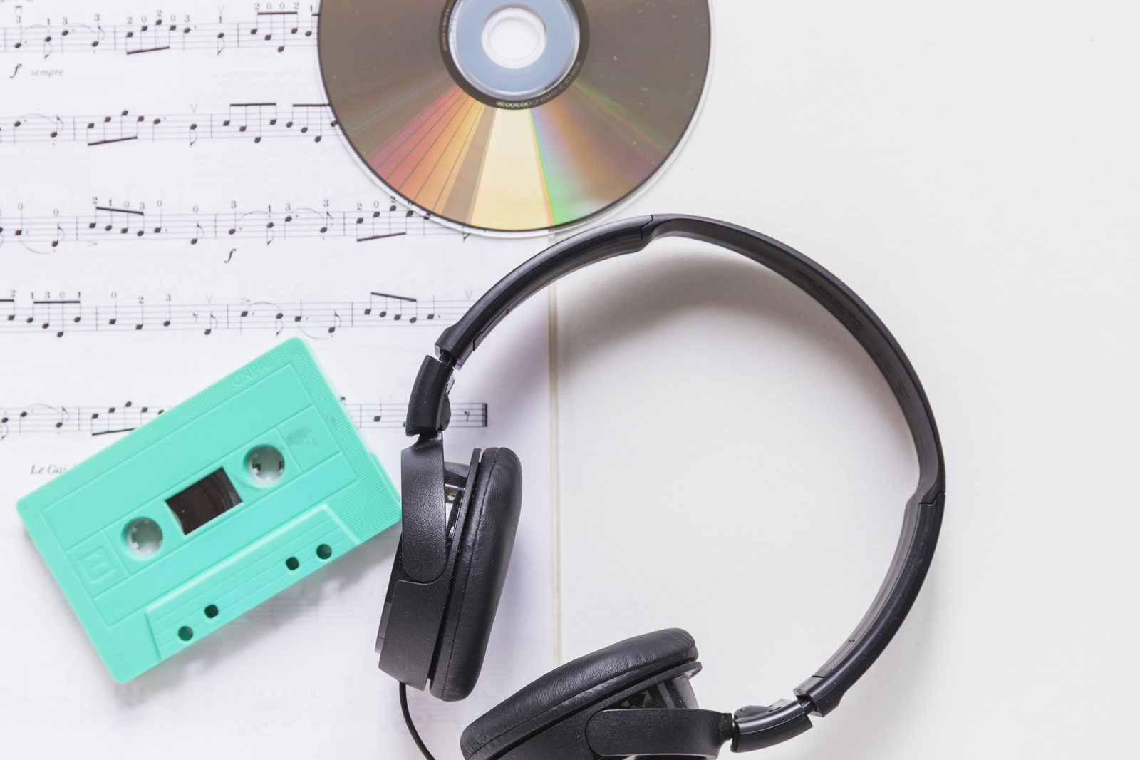 Headphones, a CD, a cassette tape, and sheet music laid out together