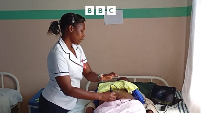 A nurse in a white uniform holds a portable ultrasound probe to a pregnant woman's belly on a hospital bed, the scan showing on a laptop beside her