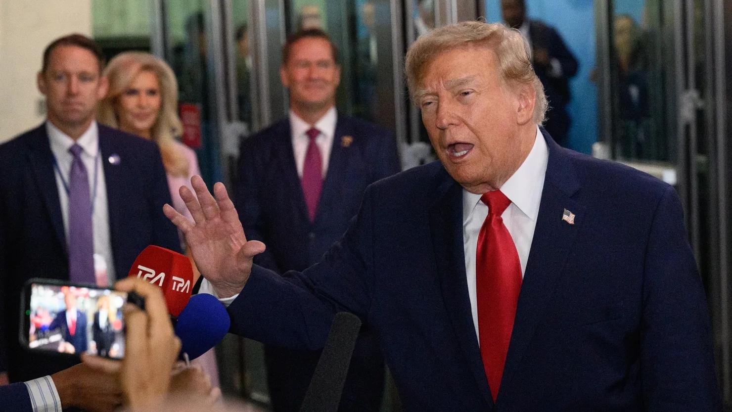 President Donald Trump gestures while speaking to reporters, surrounded by aides