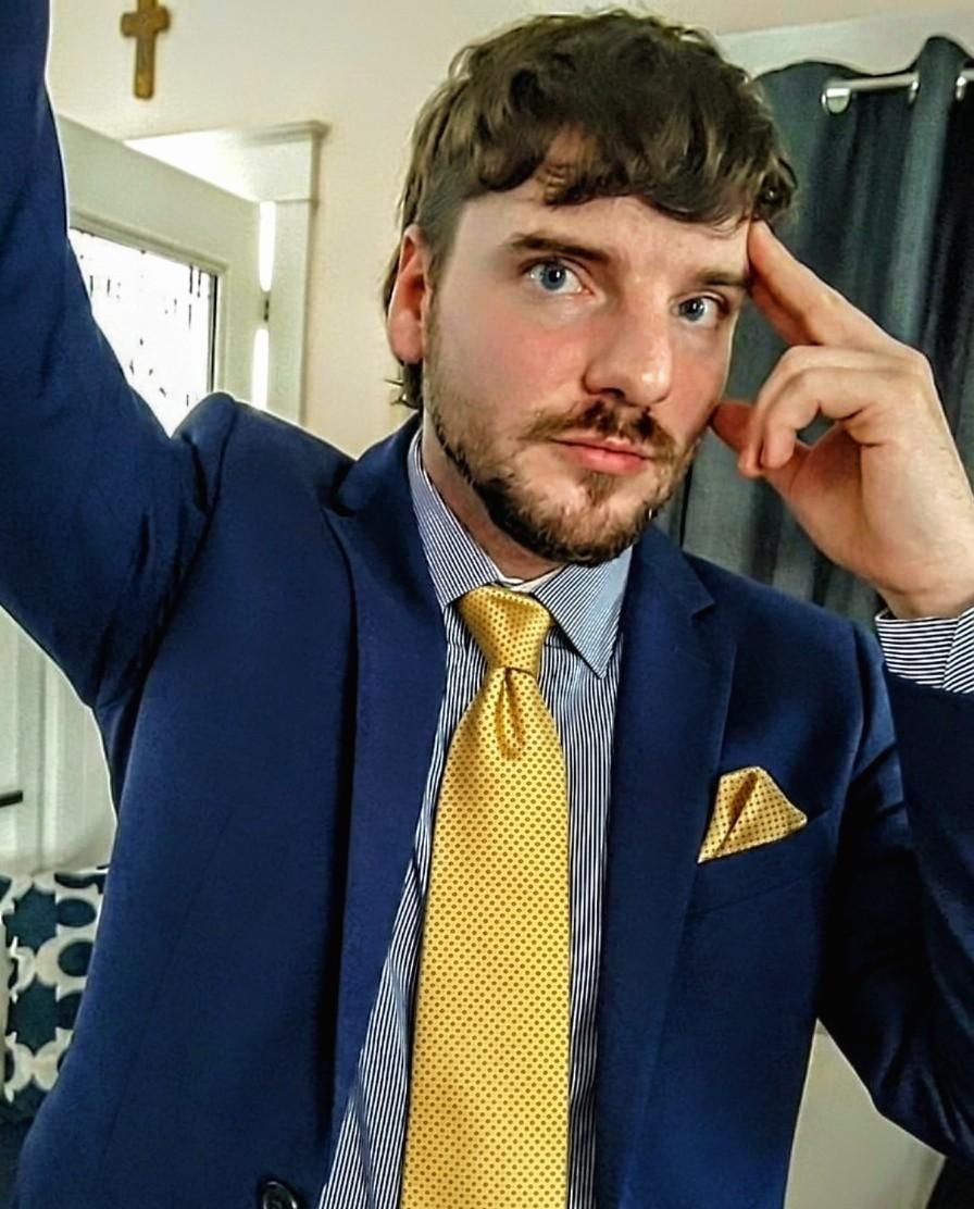 Christopher T. Bruckmann, wearing a navy suit and yellow tie, gestures thoughtfully